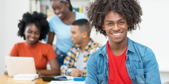 Studenten achter computer en 1 student kijkt lachend de camera in