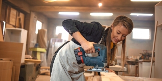 Jonge vrouwelijke student met een zaagmachine in werkplaats